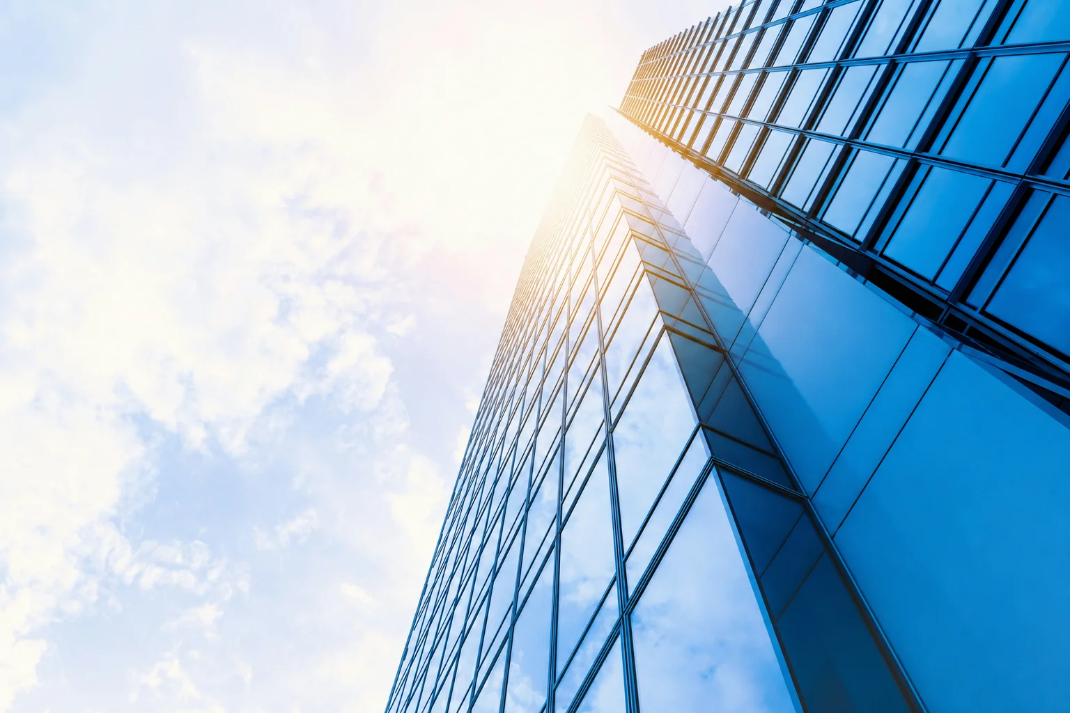 Modern glass office tower viewed from below against a bright sky